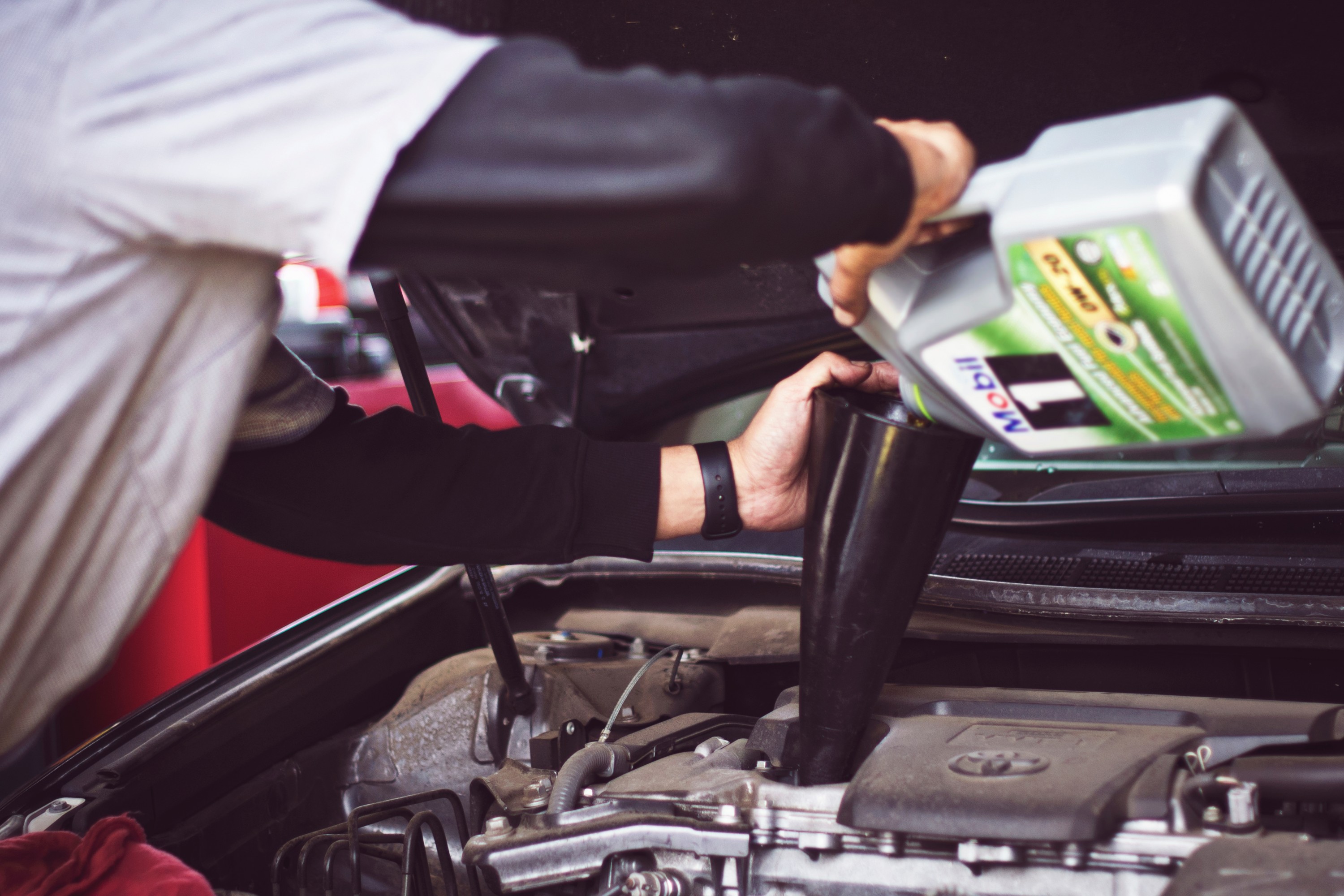 auto mechanic refilling motor oil in car engine 